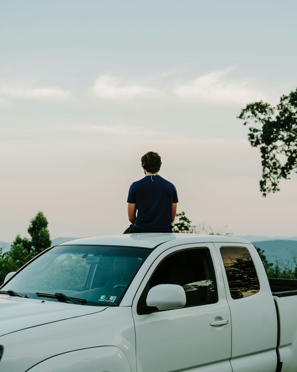 homme en chemise bleue debout à côté d’un SUV blanc pendant la journée