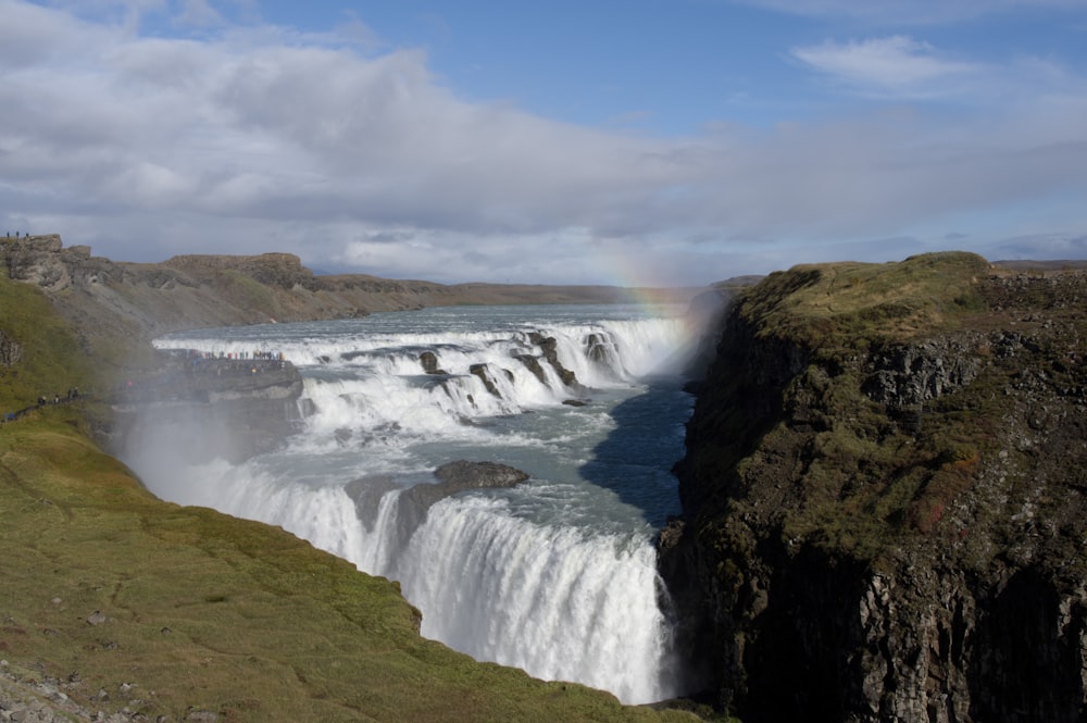 waterfalls on green grass field under white clouds and blue sky during daytime