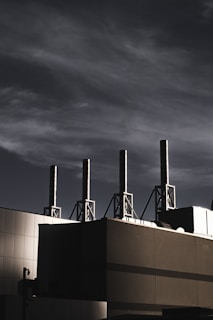 A building with several tall smokestacks against a dramatic, cloudy sky, capturing an industrial and modern atmosphere.