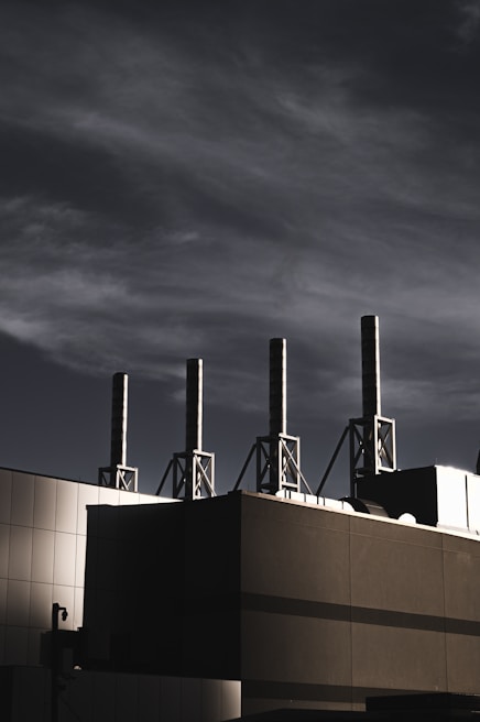 A building with several tall smokestacks against a dramatic, cloudy sky, capturing an industrial and modern atmosphere.