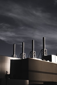 A building with several tall smokestacks against a dramatic, cloudy sky, capturing an industrial and modern atmosphere.
