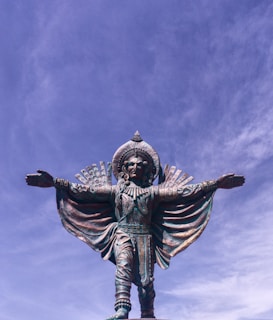 A large bronze sculpture of a human figure standing majestically in a sunlit outdoor setting.