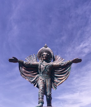 A large bronze sculpture of a human figure standing majestically in a sunlit outdoor setting.