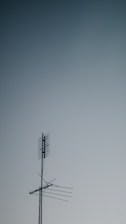 A metallic television antenna with several horizontal rods and a mesh grid atop extends against a gradient sky background that transitions from light to darker blue.