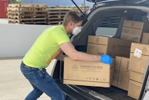 man in green t-shirt and blue denim jeans holding brown cardboard box