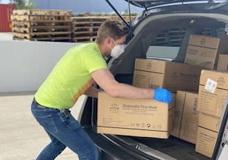 man in green t-shirt and blue denim jeans holding brown cardboard box