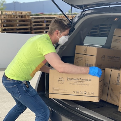 man in green t-shirt and blue denim jeans holding brown cardboard box