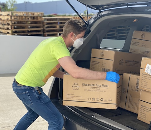 man in green t-shirt and blue denim jeans holding brown cardboard box