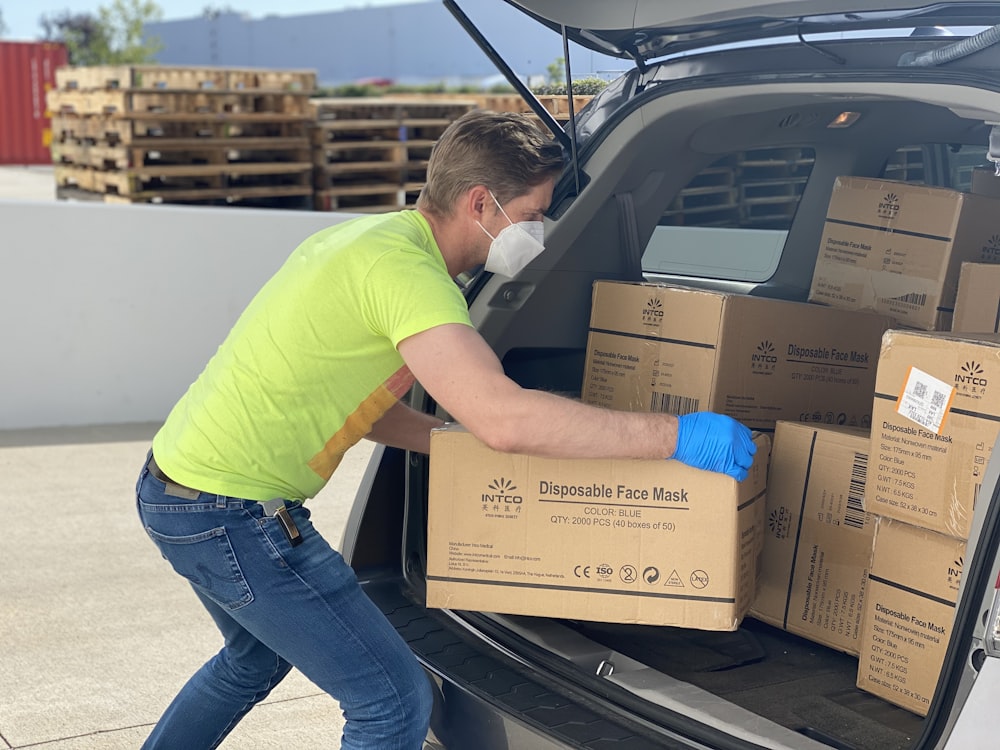 Hombre con camiseta verde y jeans de mezclilla azul sosteniendo una caja de cartón marrón