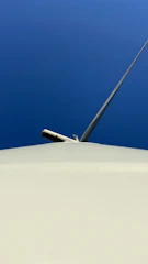 A wind turbine technician inspecting turbine blades against a clear blue sky.