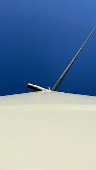 A wind turbine technician inspecting turbine blades against a clear blue sky.
