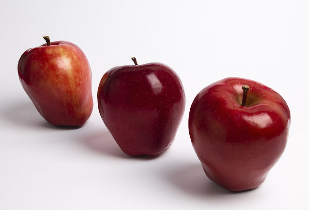 3 red apples on white surface