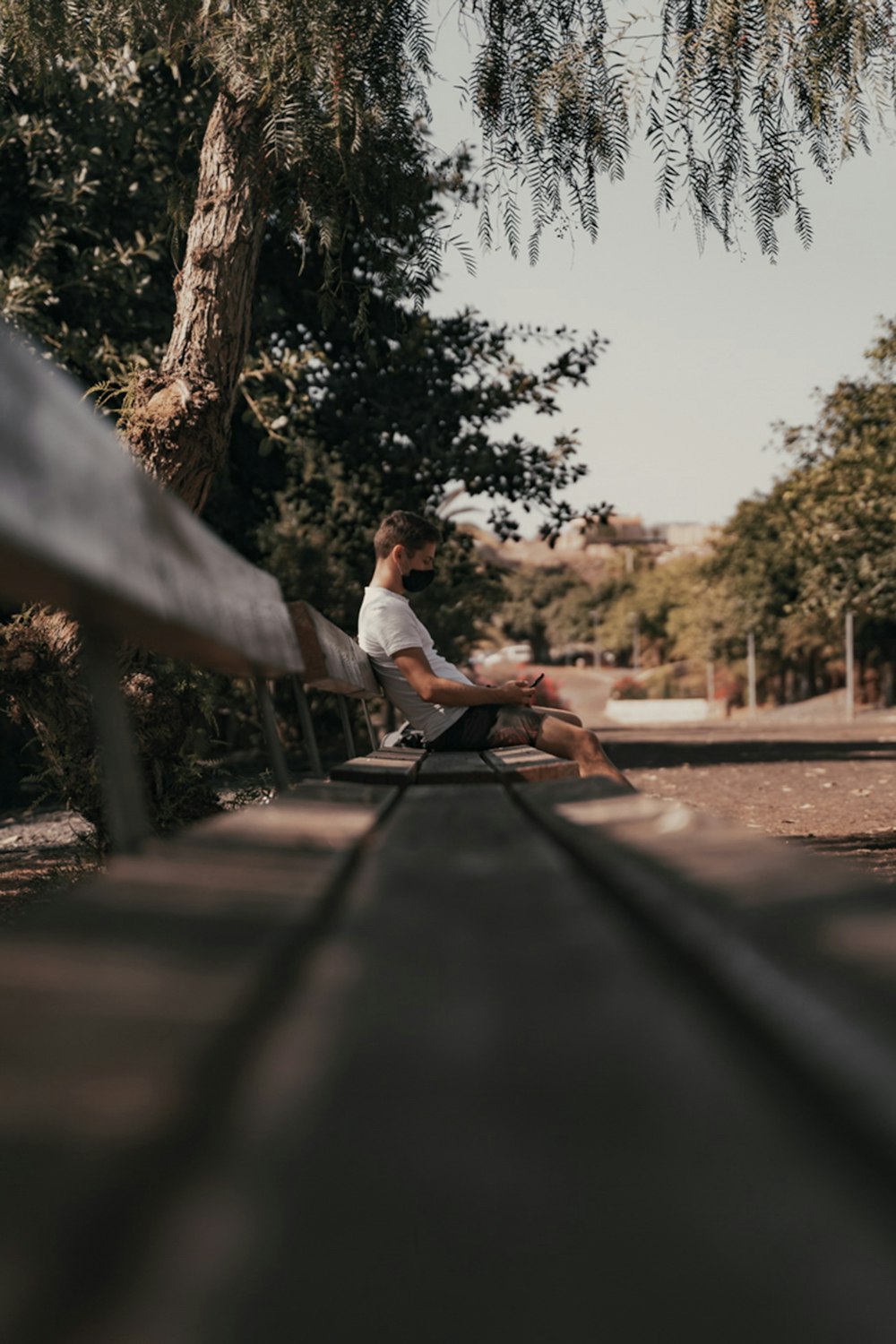 man in white dress shirt sitting on brown wooden bench during daytime