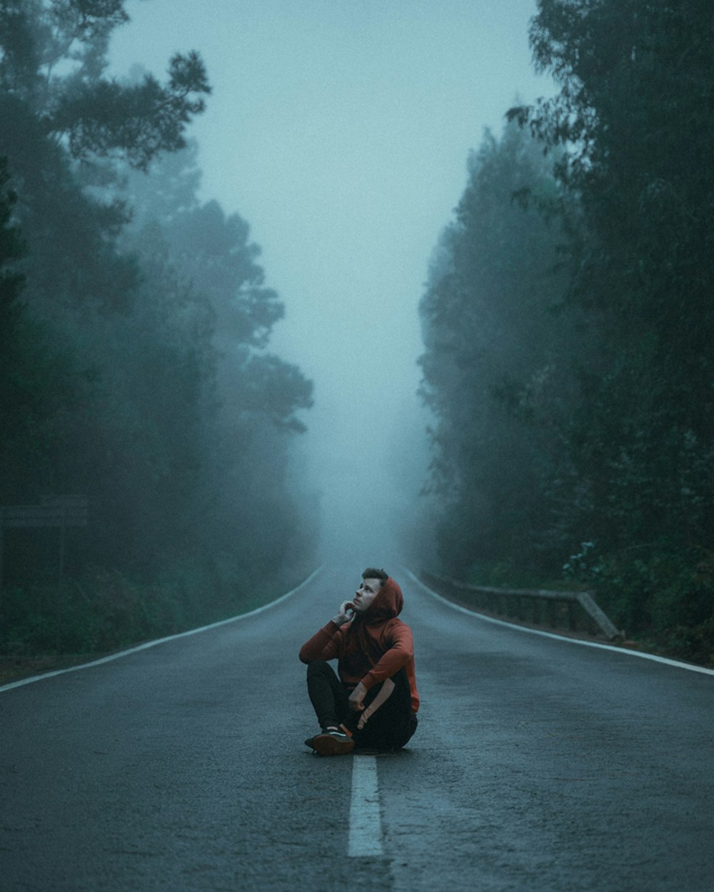man in red jacket sitting on road during foggy weather
