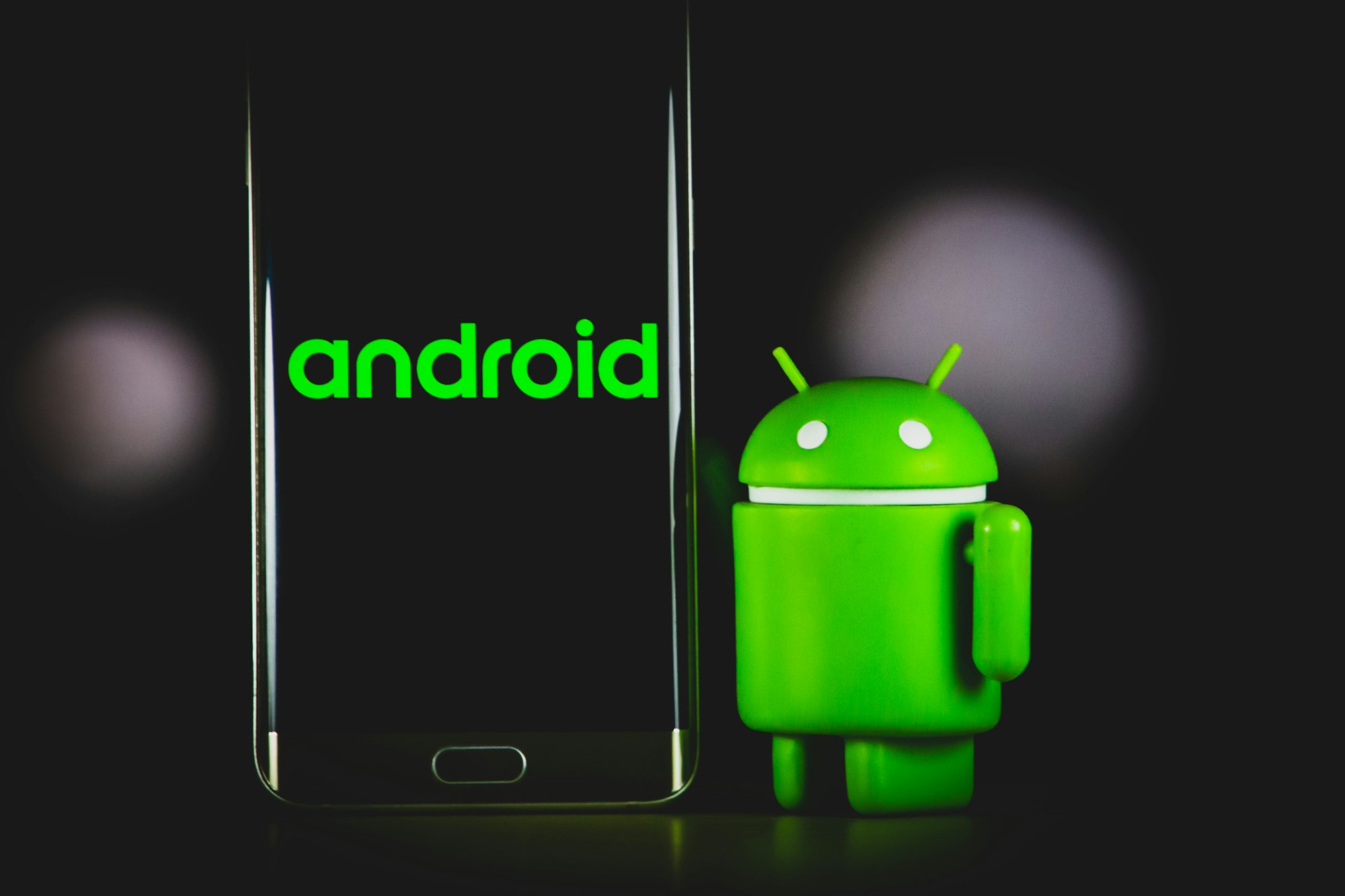 Figura de Android de color verde al lado de un smartphone