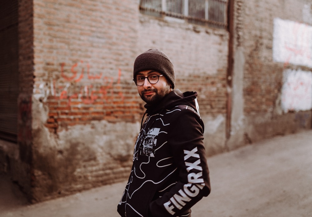 man in black and white hoodie standing near brown brick wall during daytime