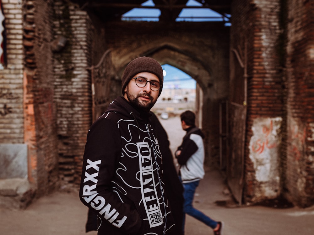 man in black hoodie standing near brown brick building during daytime