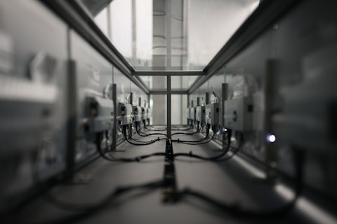 A symmetrical view of a server room or data center aisle with multiple server racks on both sides. The cabling is neatly arranged, and the environment appears dimly lit. The perspective converges at the center, creating a sense of depth.