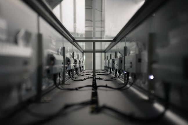 A symmetrical view of a server room or data center aisle with multiple server racks on both sides. The cabling is neatly arranged, and the environment appears dimly lit. The perspective converges at the center, creating a sense of depth.