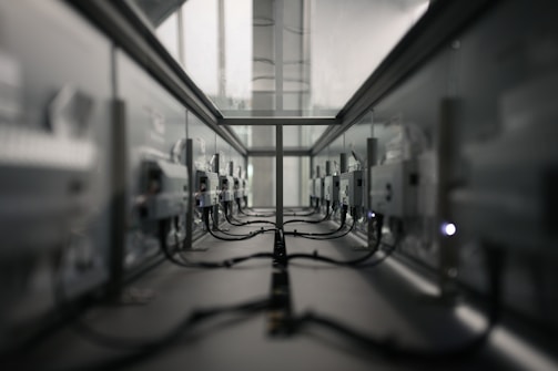 A symmetrical view of a server room or data center aisle with multiple server racks on both sides. The cabling is neatly arranged, and the environment appears dimly lit. The perspective converges at the center, creating a sense of depth.