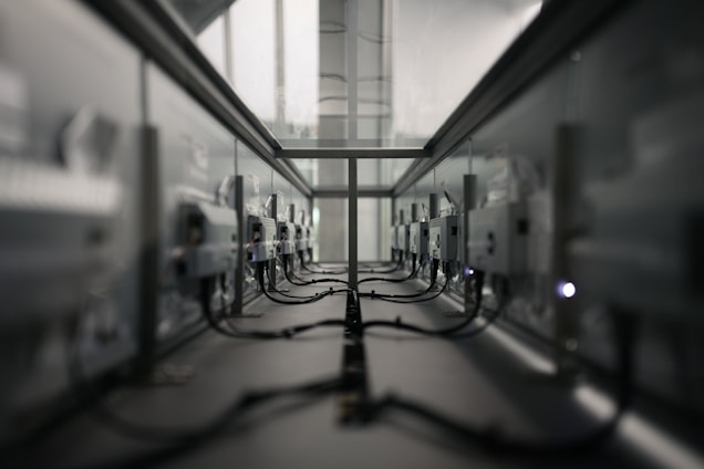 A symmetrical view of a server room or data center aisle with multiple server racks on both sides. The cabling is neatly arranged, and the environment appears dimly lit. The perspective converges at the center, creating a sense of depth.