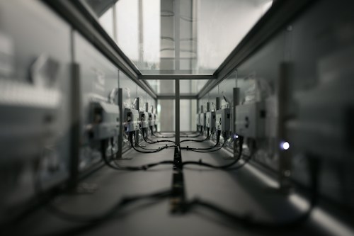 A symmetrical view of a server room or data center aisle with multiple server racks on both sides. The cabling is neatly arranged, and the environment appears dimly lit. The perspective converges at the center, creating a sense of depth.