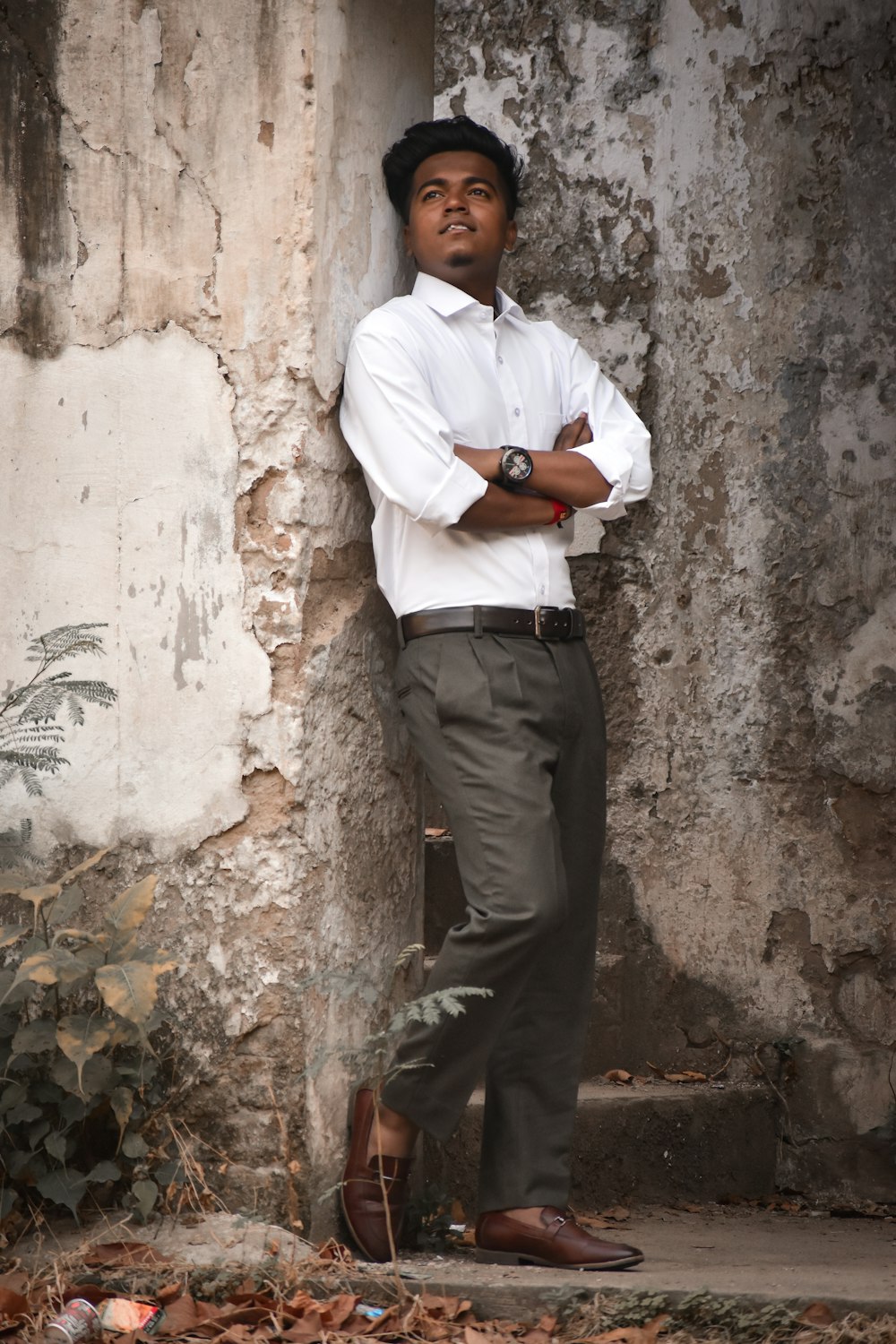 man in white dress shirt and gray pants standing beside white concrete wall during daytime