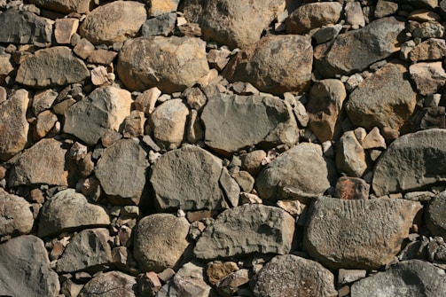 A wall constructed from an assortment of irregularly shaped stones varies in size and color. The stones are tightly packed together, displaying a range of textures and natural patterns.