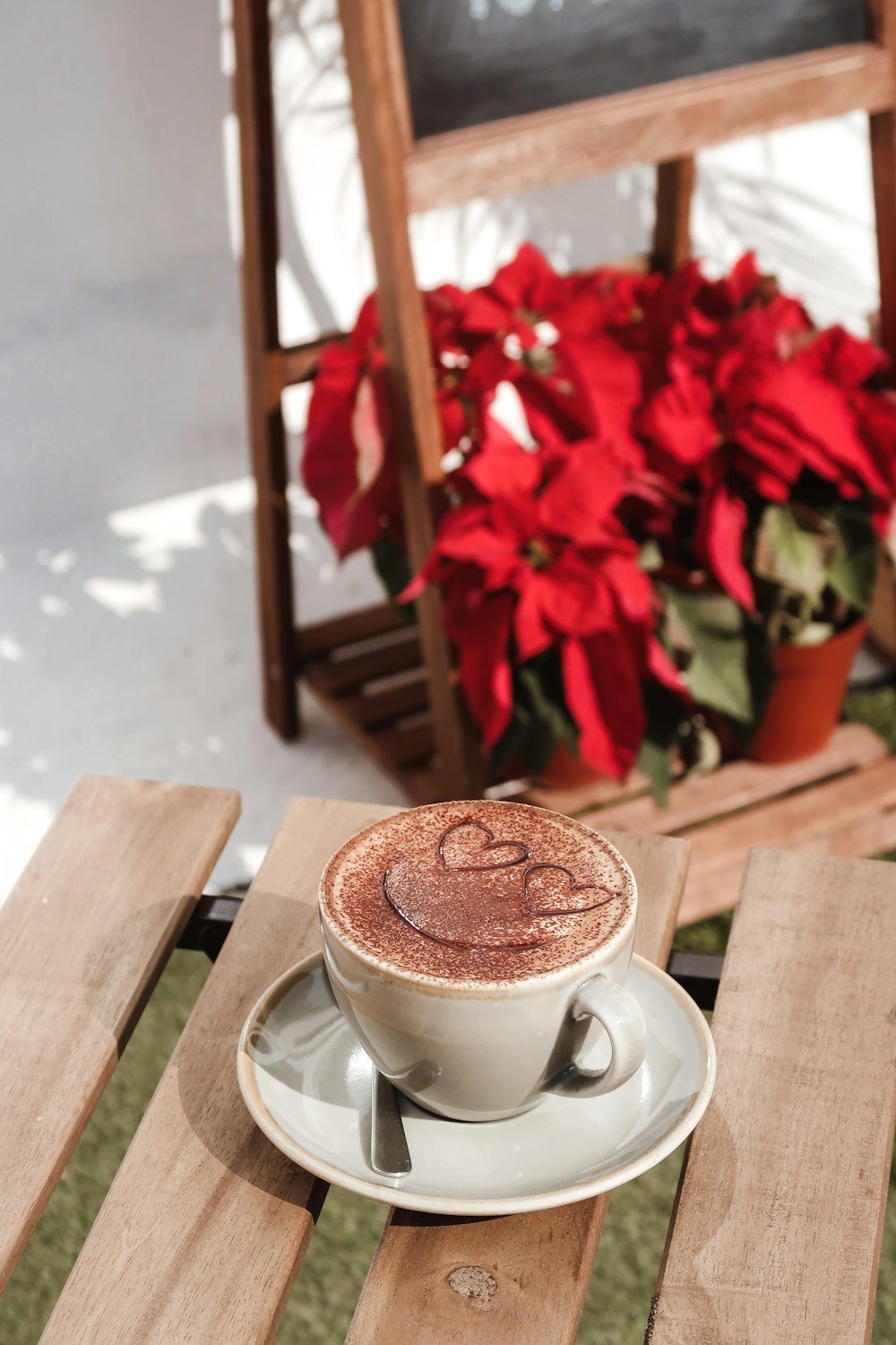 Tasse à thé en céramique blanche sur soucoupe à côté de fleurs rouges