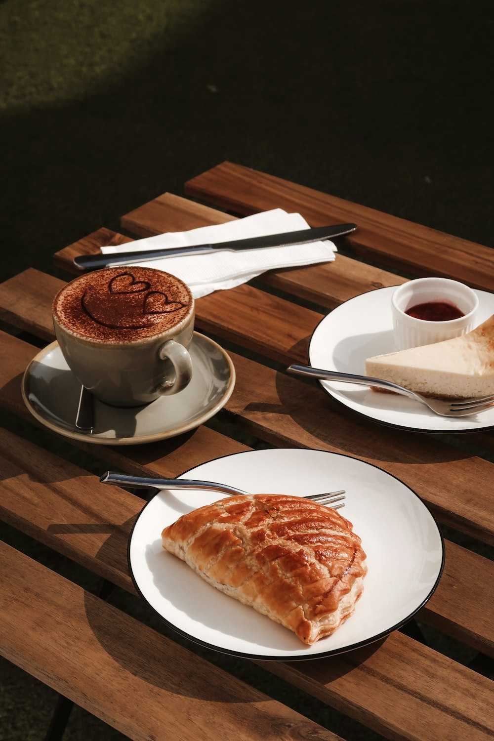 weiße Keramik-Teetasse auf weißer Keramikuntertasse neben Edelstahllöffel auf braunem Holztisch