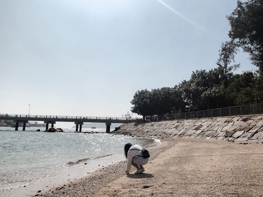 Hombre con camiseta blanca y pantalones cortos marrones sentado en un muelle de madera marrón durante el día