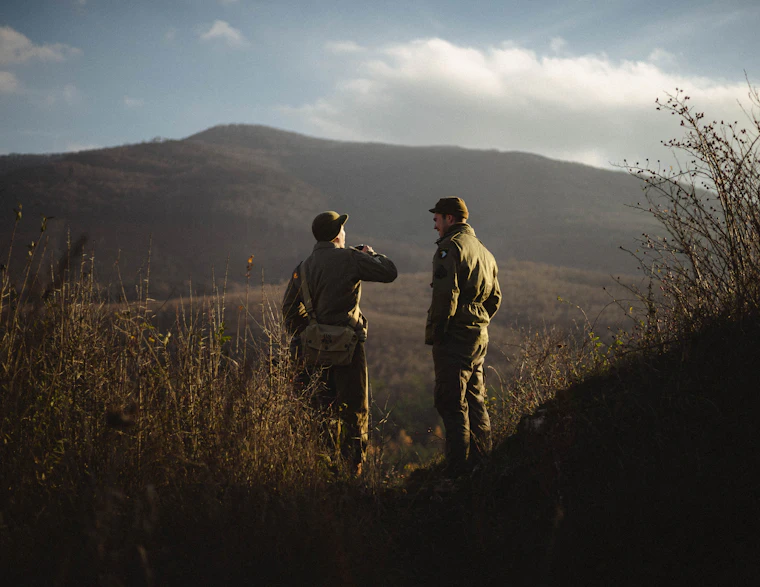 Two hunters walking a brown tundra ridge with rifles at last light