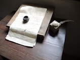 A vintage setting with a handwritten manuscript placed on a wooden desk. Beside it lies an ink pot and an old-fashioned quill pen. The lighting is soft, highlighting the weathered texture of the paper and the age of the objects.