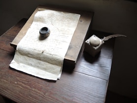 A vintage quill and inkpot casting a soft shadow on a wooden desk.