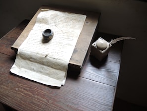 A detailed sketch of the fictional author character seated at an ancient wooden desk, surrounded by scattered parchment and quills.