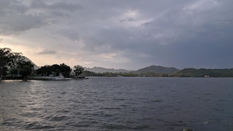 A serene lakeside view with mist rising over calm waters and distant forested hills.