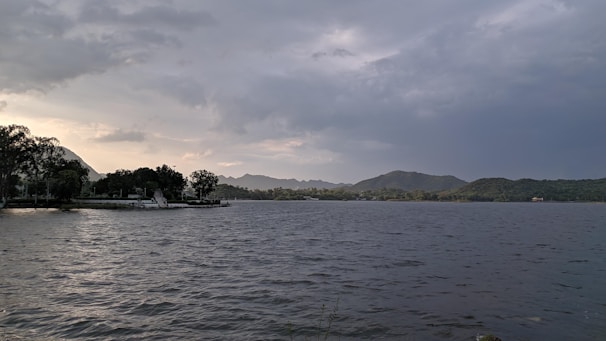 A serene lakeside view with mist rising over calm waters and distant forested hills.