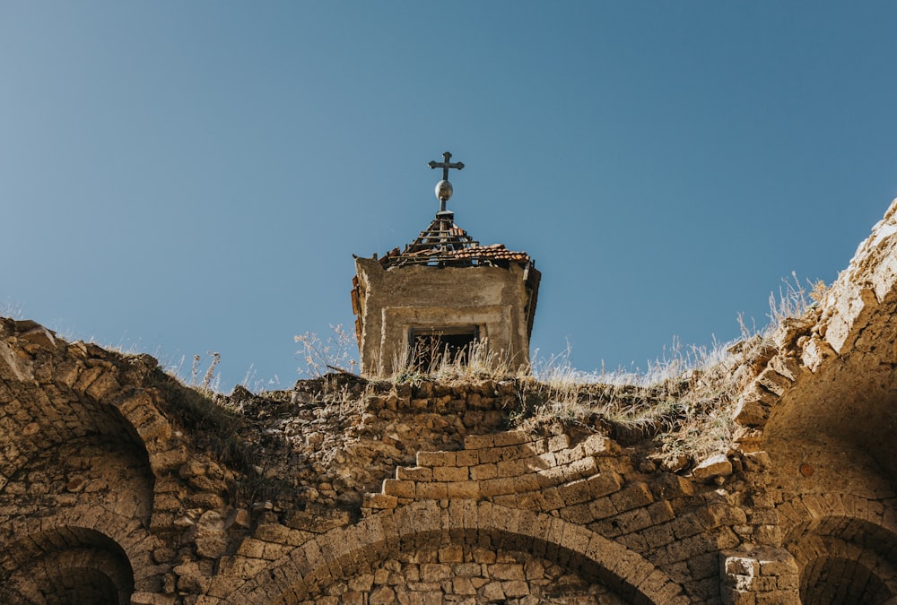 cruz de concreto cinza no topo da formação rochosa marrom sob o céu azul durante o dia