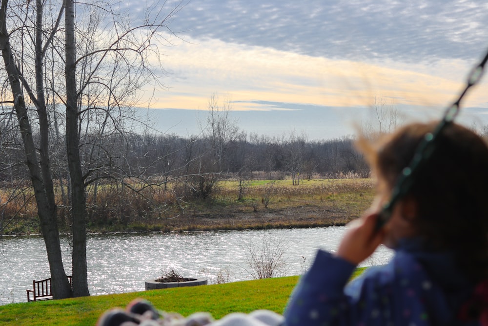 person in black shirt sitting on green grass field near river during daytime