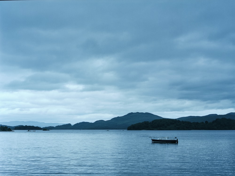 boat on sea near mountain under cloudy sky during daytime