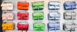 A display of colorful handbags in three rows on a perforated white wall, each row showcasing bags in different shades such as orange, green, blue, red, yellow, and beige.