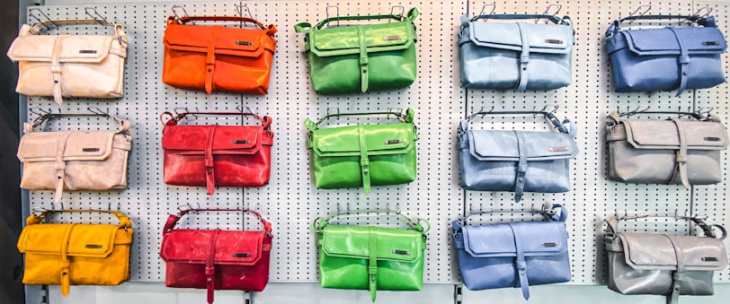 A display of colorful handbags in three rows on a perforated white wall, each row showcasing bags in different shades such as orange, green, blue, red, yellow, and beige.