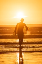 silhouette of man holding surfboard on beach during sunset