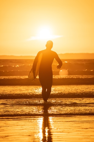 silhouette of man holding surfboard on beach during sunset