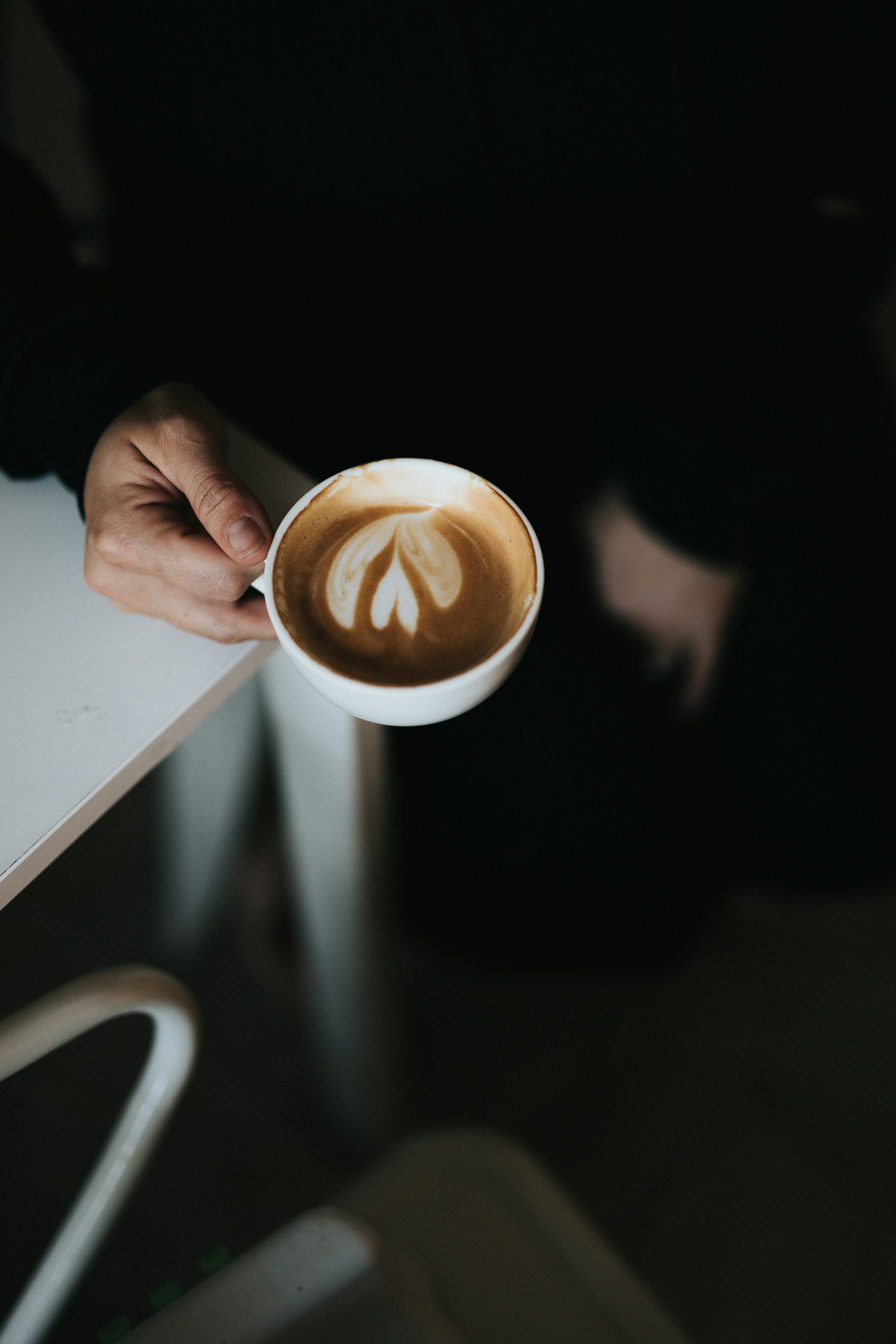 person holding white ceramic mug with brown liquid