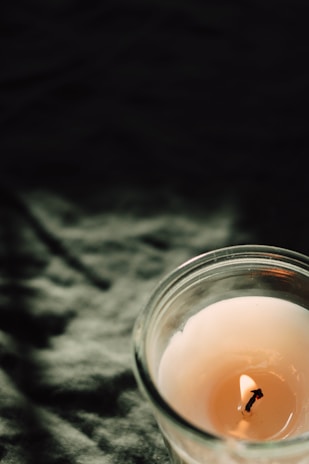 Close-up of a handcrafted scented candle glowing softly on a beige linen cloth.