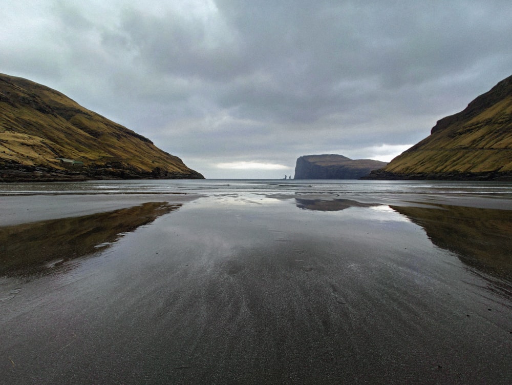 body of water near mountain under cloudy sky during daytime