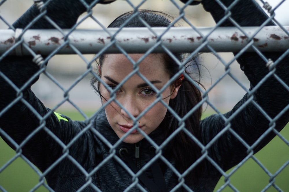 woman in black jacket leaning on gray metal fence