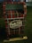 A decorative mailbox is adorned with a red and green plaid pattern and is labeled 'North Pole Airmail Express Service'. It is situated outdoors on a grass surface.