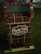 A decorative mailbox is adorned with a red and green plaid pattern and is labeled 'North Pole Airmail Express Service'. It is situated outdoors on a grass surface.